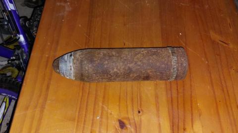 An old mortar shell rests on a wooden table. Its body has rusted.