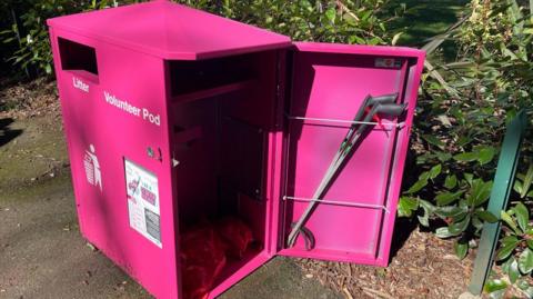 Open-doored pink-coloured litter-picking pod in Sheffield Park, Scunthorpe, with two grabbers slotted into wires on the back of the door