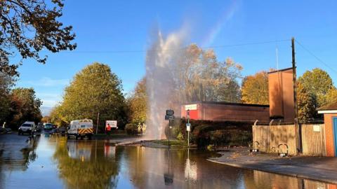 A burst water pipe with water shooting out from the ground outside a small fire station in East Leake in Nottinghamshire.
