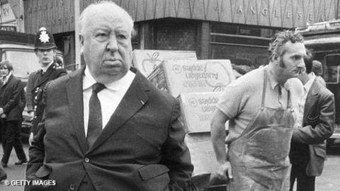 Alfred Hitchcock stands in a busy street