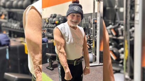 A man wearing a grey bobble-hat, sleeveless T-shirt and black gym shorts.