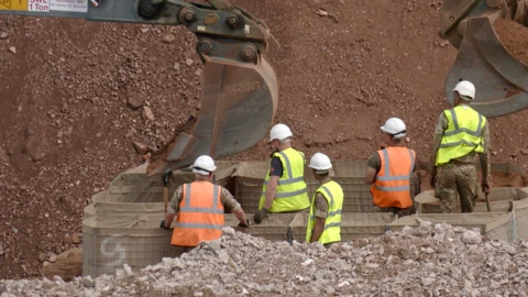 Five people in Army fatigues and high-vis jackets with white hat in a hole