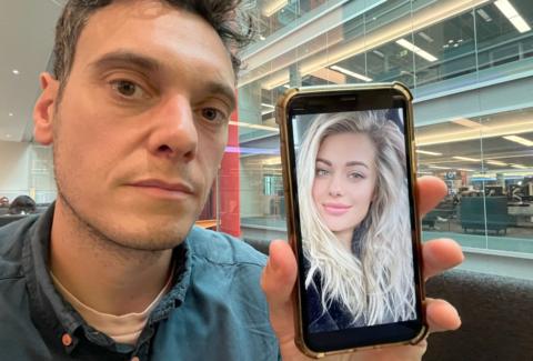 Joe Tidy holding a phone with the picture of a blonde woman