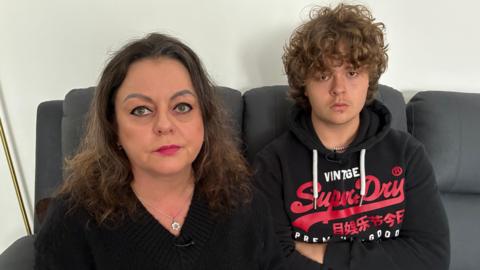 Wioletta (left) with brown curly hair, wearing a black top, and Alex (right) with brown curly hair, wearing a black SuperDry jumper with red writing.