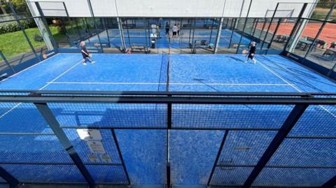 A blue padel court with two players on it. 