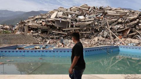 a man walks by rubble and the remnants of a swimming pool near the site of the quake.