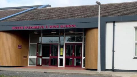 The entrance of the school with red lettering reading Queen Elizabeth II High School.