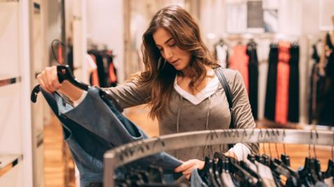 Woman holding up an item of clothing in a shop