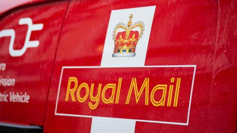 The side of a Royal Mail van with its logo, including an image of a crown above the words "Royal Mail" in yellow on a red background