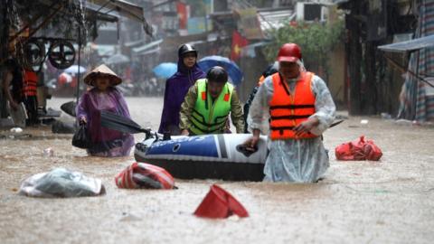 People walk knee-deep pulling an inflatable raft in a street flooded with water in Hanoi, Vietnam