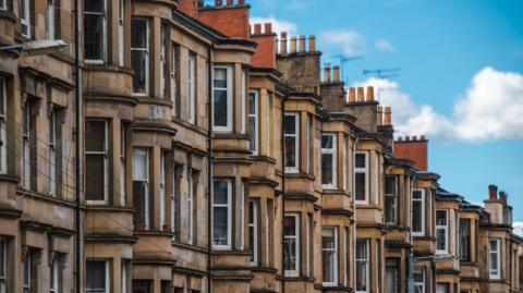 A row of sandstone tenement flats with a bright blue sky in the top right of the frame