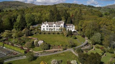 An aerial view of Brockhole-on-Windermere. A large white building is surrounded by gardens and trees.