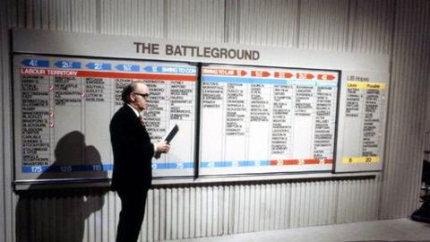 Robert McKenzie stands in front of the Election 'Battleground' Board showing Conservatives, Labours and Liberals seat gains and losses.