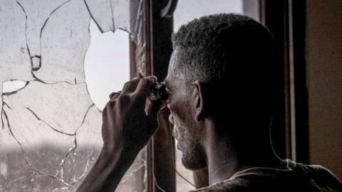 A Sudanese army soldier scans the frontline with binoculars in Khartoum North in December. He is looking out of broken window of a building.
