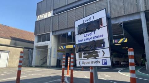 Image of the outside of a multi-storey car park with a sign to different levels covered in black tape.