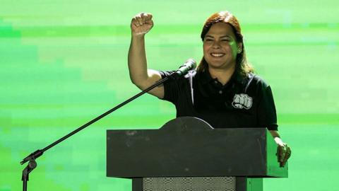 Sara Duterte pumping her fist in the air at a podium