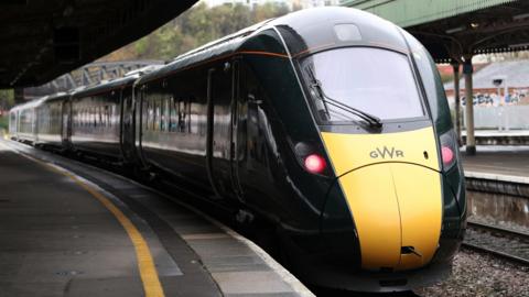 The front of a yellow and black Great Western Railway train parked at a station. There is nobody on the platform