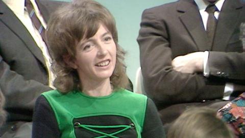 A woman in a green and black top speaking in the audience.