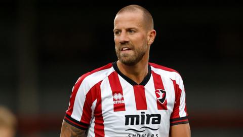 Harry Pell standing on the pitch wearing Cheltenham Town kit during a match this season