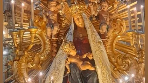 Our Lady of Grace in Nettuno, a wooden statue of the Madonna, wearing a crown, a white veil, dressed in red and blue and holding an infant Christ on her lap. She is sitting on a gilded throne beneath a golden canopy. 