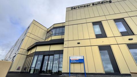 The Dartmoor Building at Plymouth's Derriford Hospital. The modern-looking three-storey structure features a combination of beige and black exterior panels. It has large windows and a glass entrance.