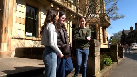 Triùir oileanaich nan seasamh còmhla air an t-sràid an Glaschu agus iad a' còmhradh ri càch a chèile. 