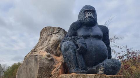 A large gorilla statue sitting on a tree stump as viewed from below.