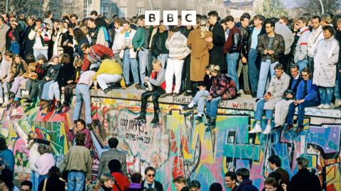 Groups of people stand on and around the Berlin Wall