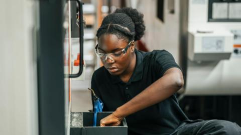 Concentrated young female worker examining mechanics while working in factory.
