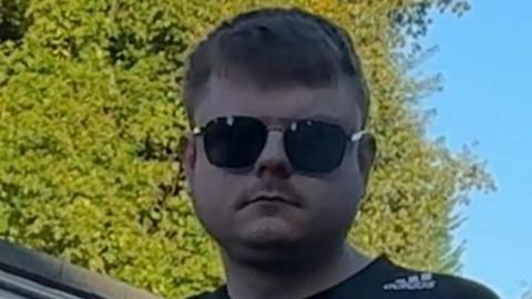 A man in his 20s with short brown hair wearing aviator sunglasses