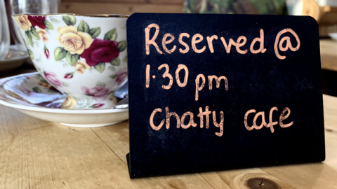 A cup and saucer and a sign reserving the table for Chatty Cafe