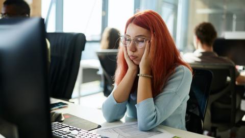 A worker feeling exhausted while working on desktop computer in the office.