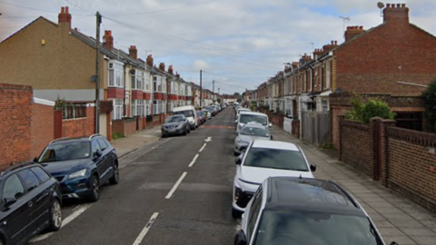 Hollam Road is a narrow one-way street with terraced two-storey houses and cars on both sides of the road.