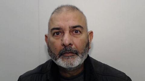 Prison headshot of Mohammed Zahid stood in front of a grey background. He is an Asian man, bald with a salt-and-pepper beard. 