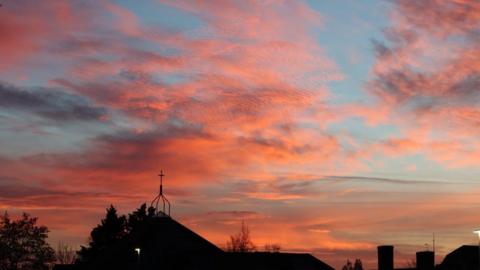 Orange and pink coloured clouds in a soft blue sky over black silhouetted buildings 