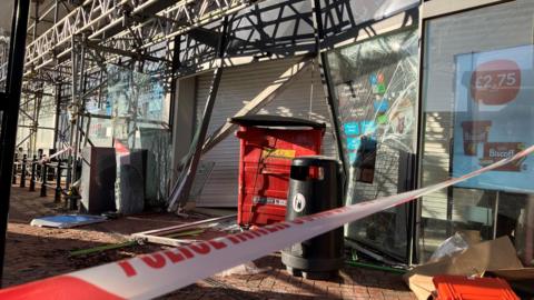 Police tape crosses a pavement outside a shuttered Co-op store, which also has scaffolding around it