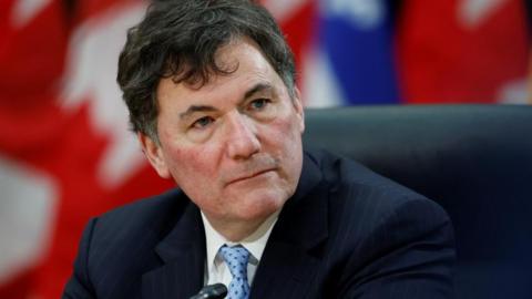 An image showing Dominic LeBlanc. He is seated and is looking at the right of the camera. He has black hair, and is is wearing a dark blue pinstriped suit with a light blue patterned tie.