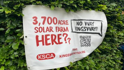 A banner which states "3,700 acre solar farm here??' and "No Way Kingsway", hung on a hedge.