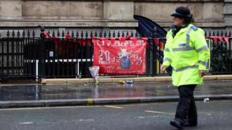 A police officer walks past a Liverpool FC flag at the site of an incident where a car ploughed into a crowd of Liverpool fans during a parade celebrating their side's Premier League title