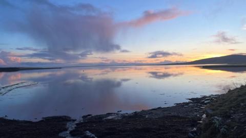 A bay with a sunset and rocks in the foreground.