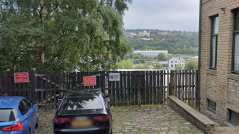 Two cars parked in front of a fence overlooking an embankment with a view over the city