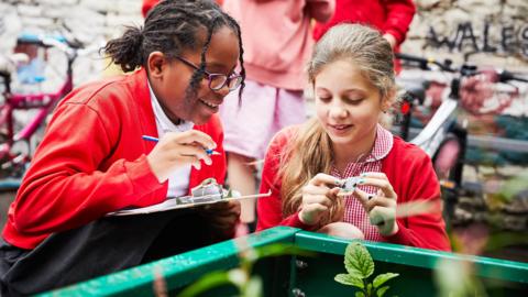 A pupil holding a micro:bit while the other holds a clipboard and pen