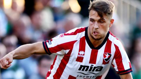 Lewis Payne in action for Cheltenham in their red and white striped home shirt