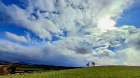 Sun trying to break through partly cloudy skies above an expanse of grassland