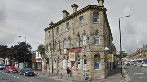 A corner building, with a red sign saying 'Victoria hotel' with people walking past on the pavement 