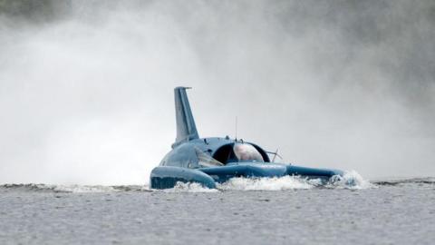 Close-up of Bluebird operating on Loch Fad. It is a craft that looks like a cross between a plane and a boat. It is painted blue. Spray is shooting up behind it.