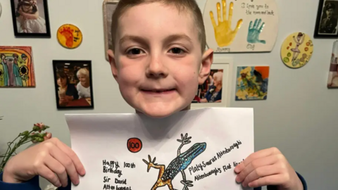 Max showing his 100th drawing of a platysaurus attenboroughi, also known as Attenborough's flat lizard. 