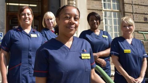 Five female nurses in navy uniforms outside QE Hospital, Birmingham