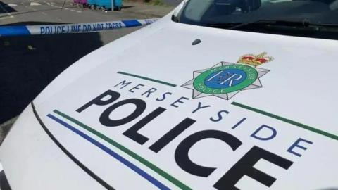 Merseyside Police vehicle inside a police cordon with blue and white police tape on a street