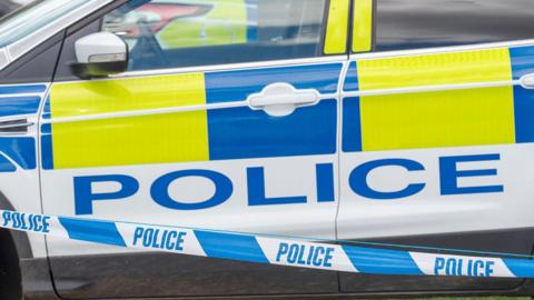 An empty, parked police car with police tape in front of it